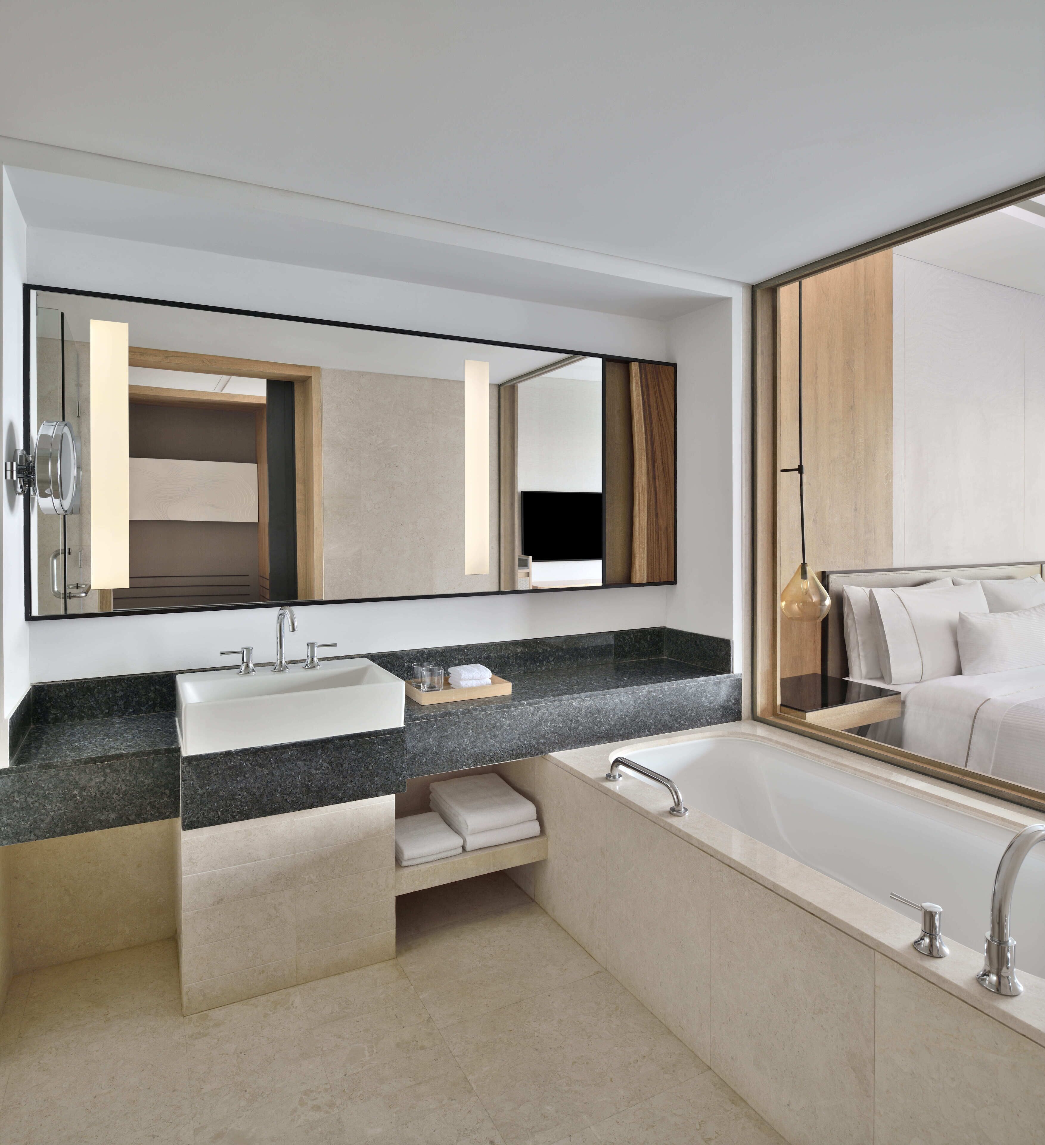 A modern bathroom with two sinks, a large mirror, a bathtub, and a wooden vanity.