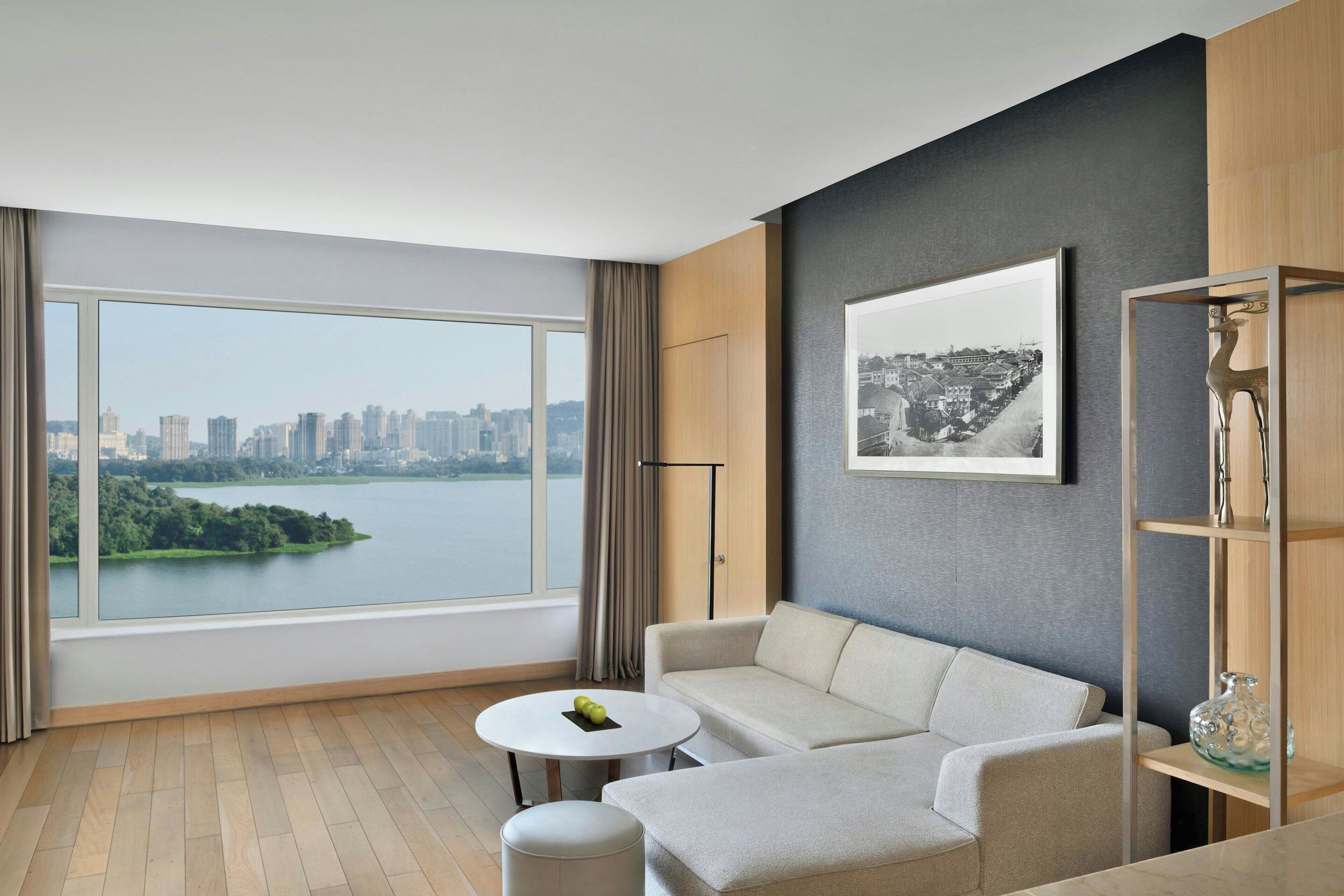 A modern living room with a large window, a sofa, a small round table, and a bookshelf.