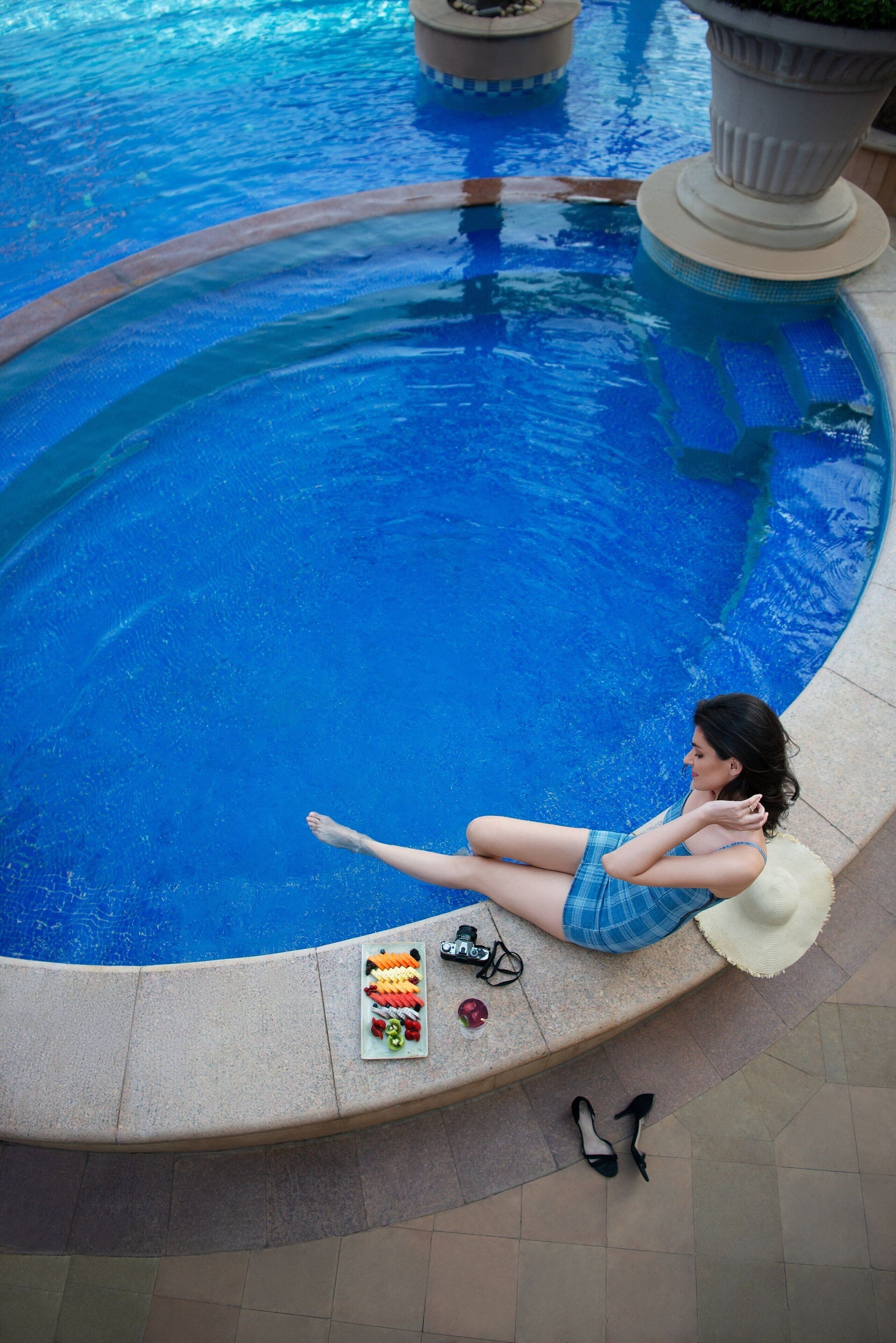 Una dona es relaxa al costat d'una piscina amb una bandeja de fruita i un barret.