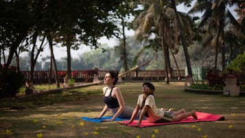 Guests can practice yoga in a serene outdoor space surrounded by trees and a fence.