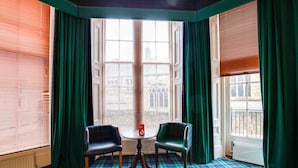 A corner room with two chairs, a small table, and a view through large windows with blinds. - Lost Guest House Stirling (Stirling)