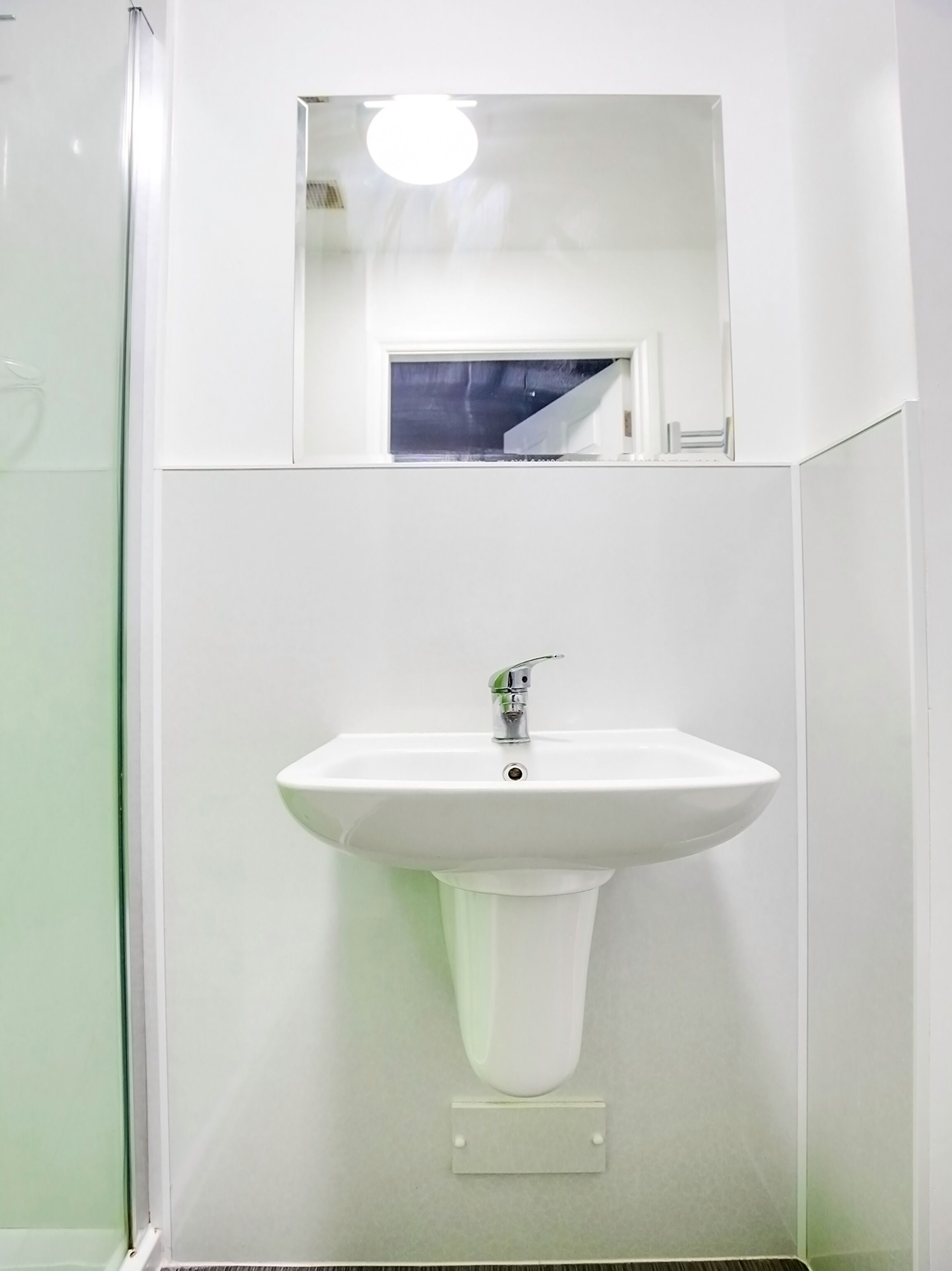 A bathroom with a white sink, a mirror above it, and a shower area.