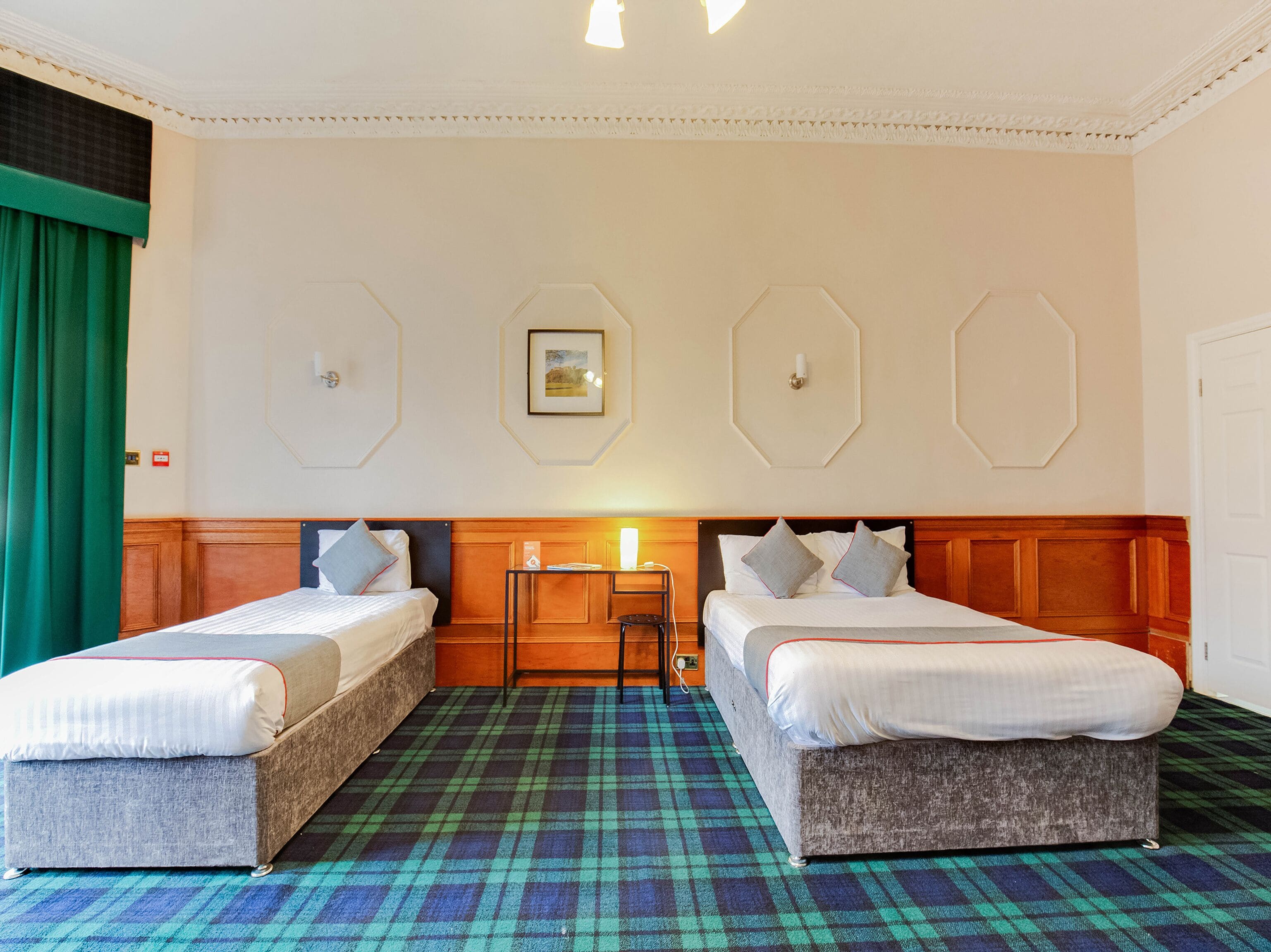 A hotel room with two beds, a check-in desk, and a patterned carpet.