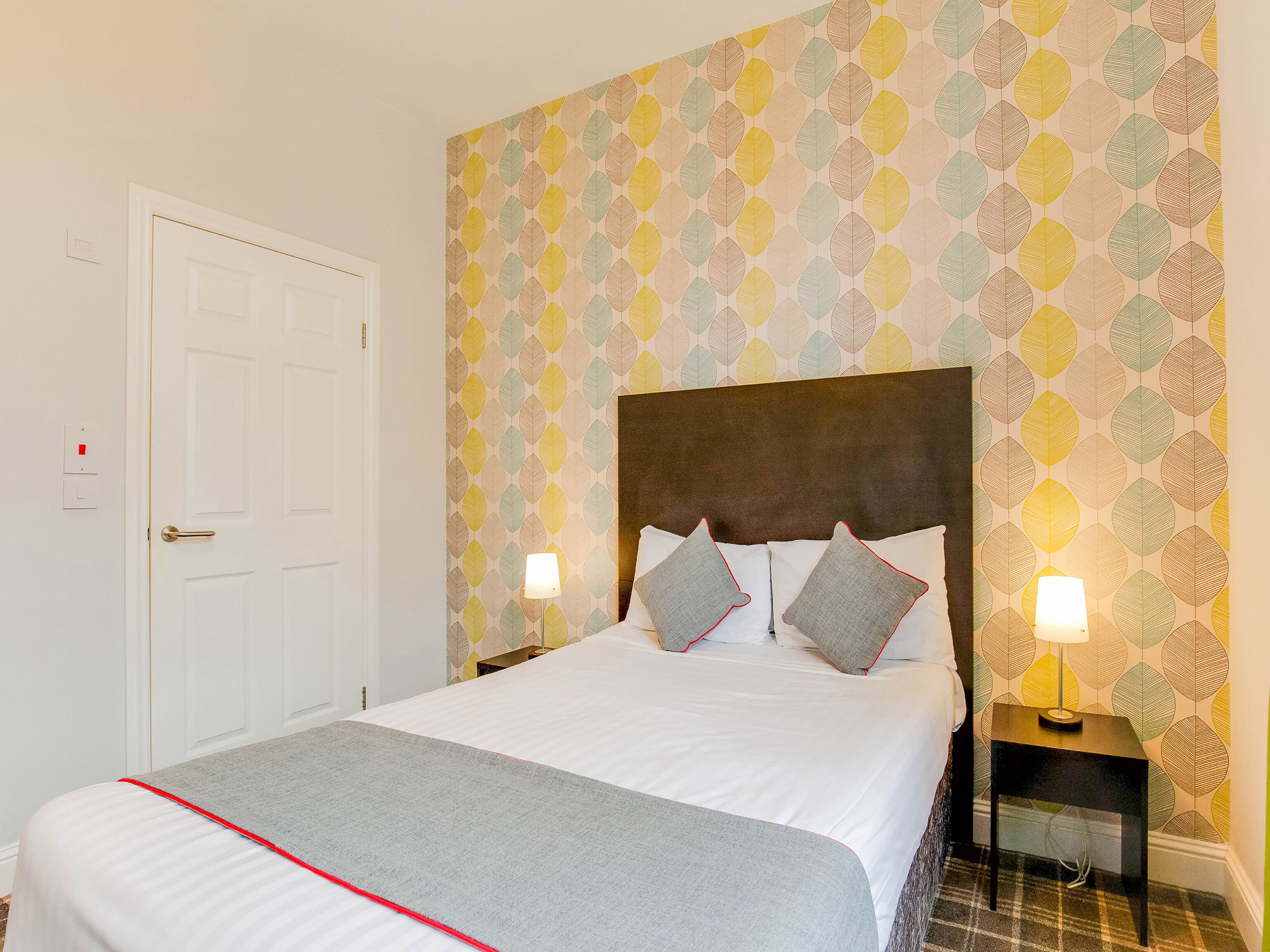 A neatly made bed with a grey blanket, a white headboard, and two bedside lamps.