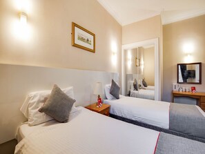 Habitación de hotel con dos camas, una mesita de noche con lámpara, un espejo y un cuadro en la pared.