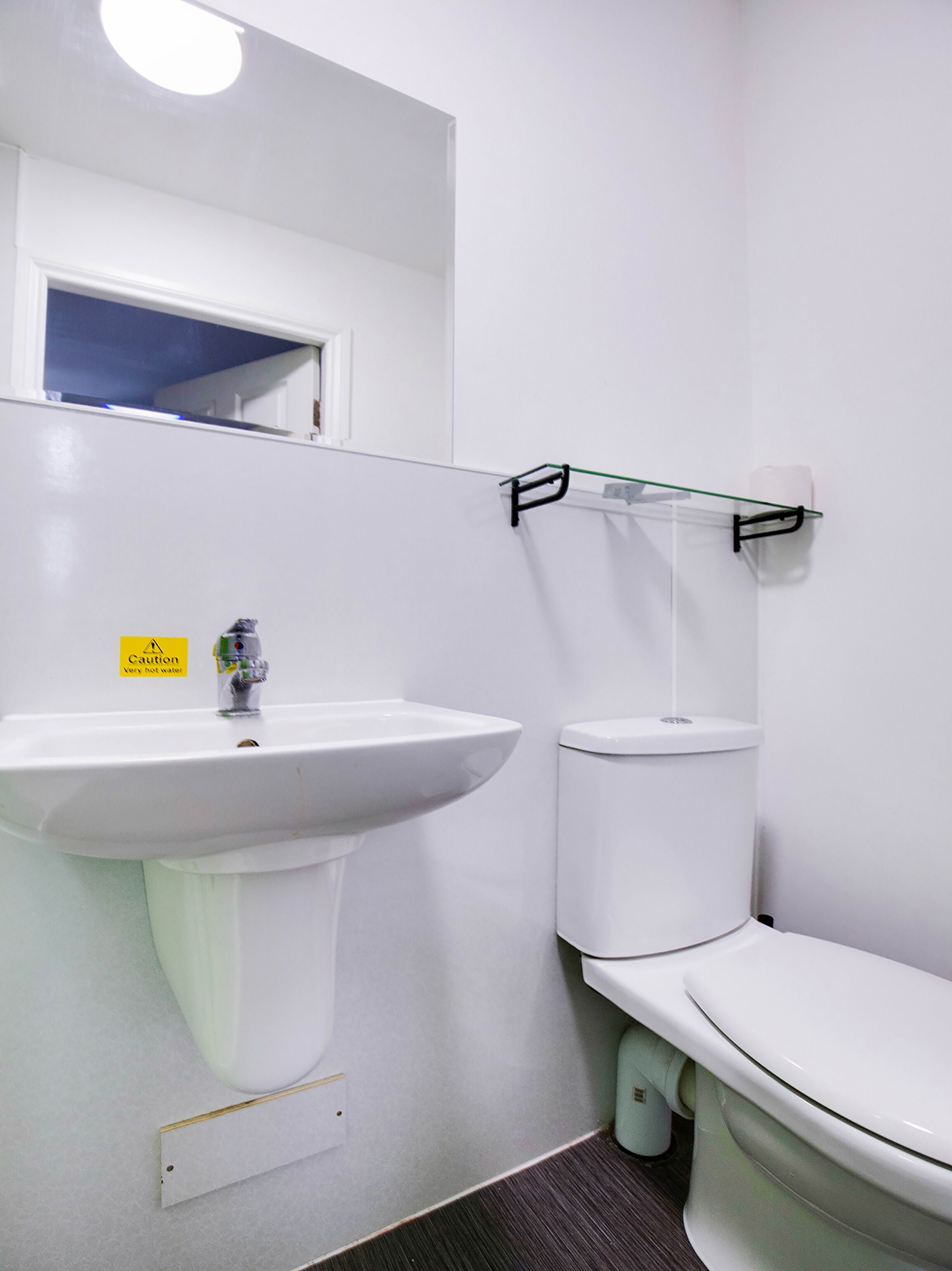 A bathroom with a white sink, toilet, and a glass shelf above the toilet.