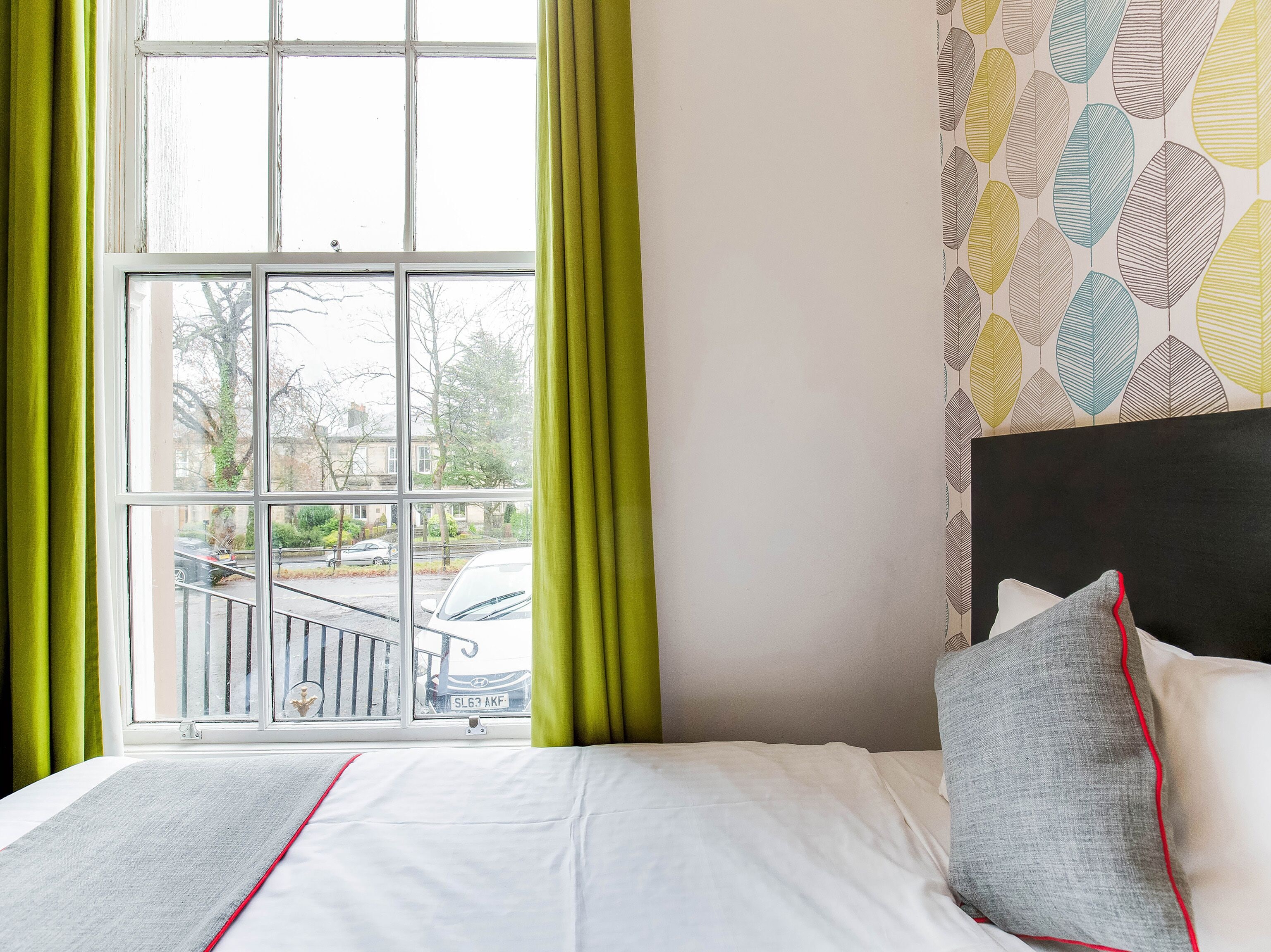A hotel room with a large window, a bed with white bedding, and a patterned wall.