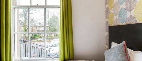 Ein Hotelzimmer mit großem Fenster, einem Bett mit weißer Bettwäsche und einer Wand mit Muster.