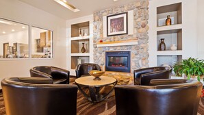 Un espace de détente moderne avec des fauteuils en cuir, une table ronde, une cheminée en pierre et des étagères ornées d’objets décoratifs.