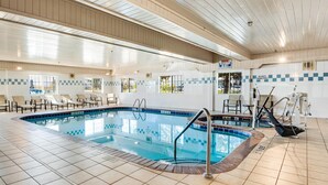Une piscine intérieure avec un sol carrelé, de grandes fenêtres laissant entrer la lumière du soleil et des chaises longues.
