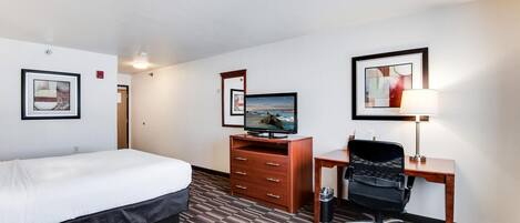 Une chambre d’hôtel avec un grand lit, un bureau avec un ordinateur, une chaise, une télévision et des œuvres d’art encadrées accrochées aux murs.