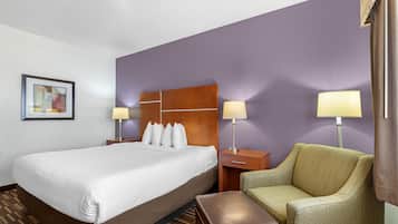 Quarto de hotel com uma cama grande, duas mesas de cabeceira com luminárias, uma poltrona verde e um banquinho marrom.