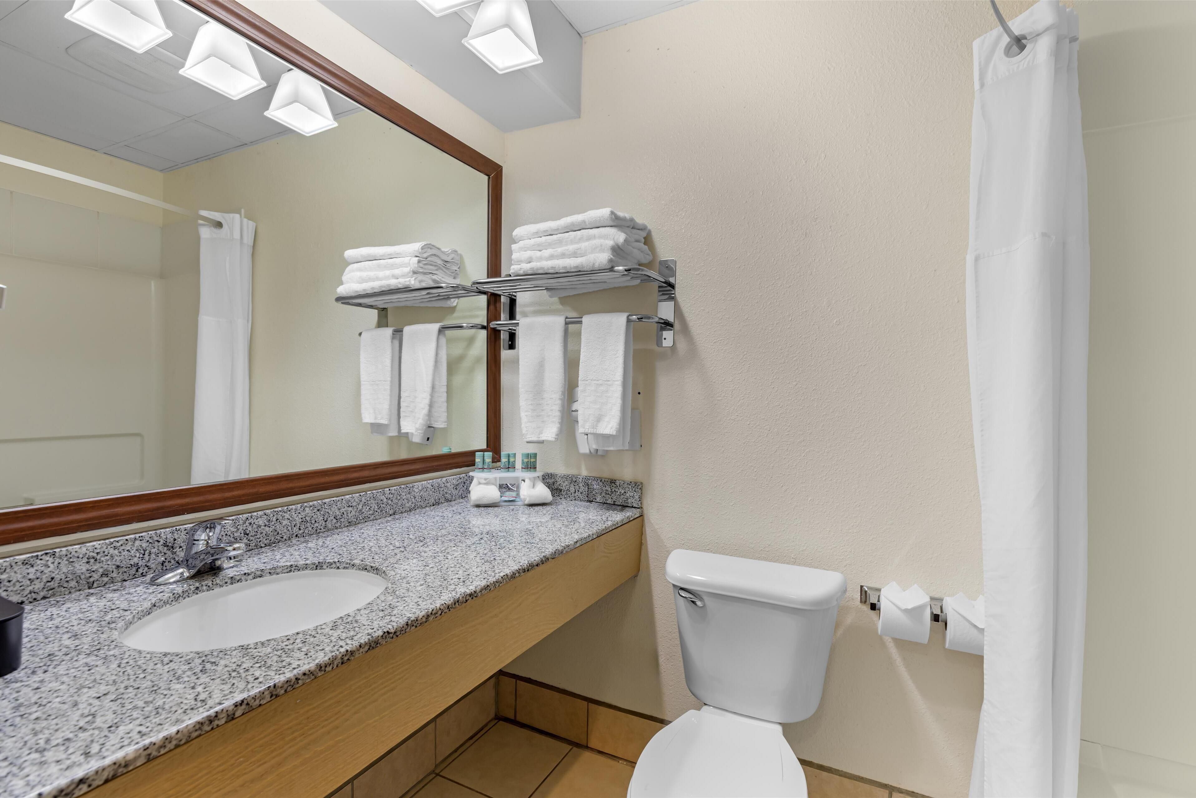 Un baño con lavamanos de encimera de granito, un inodoro blanco y un perchero con toallas dobladas.