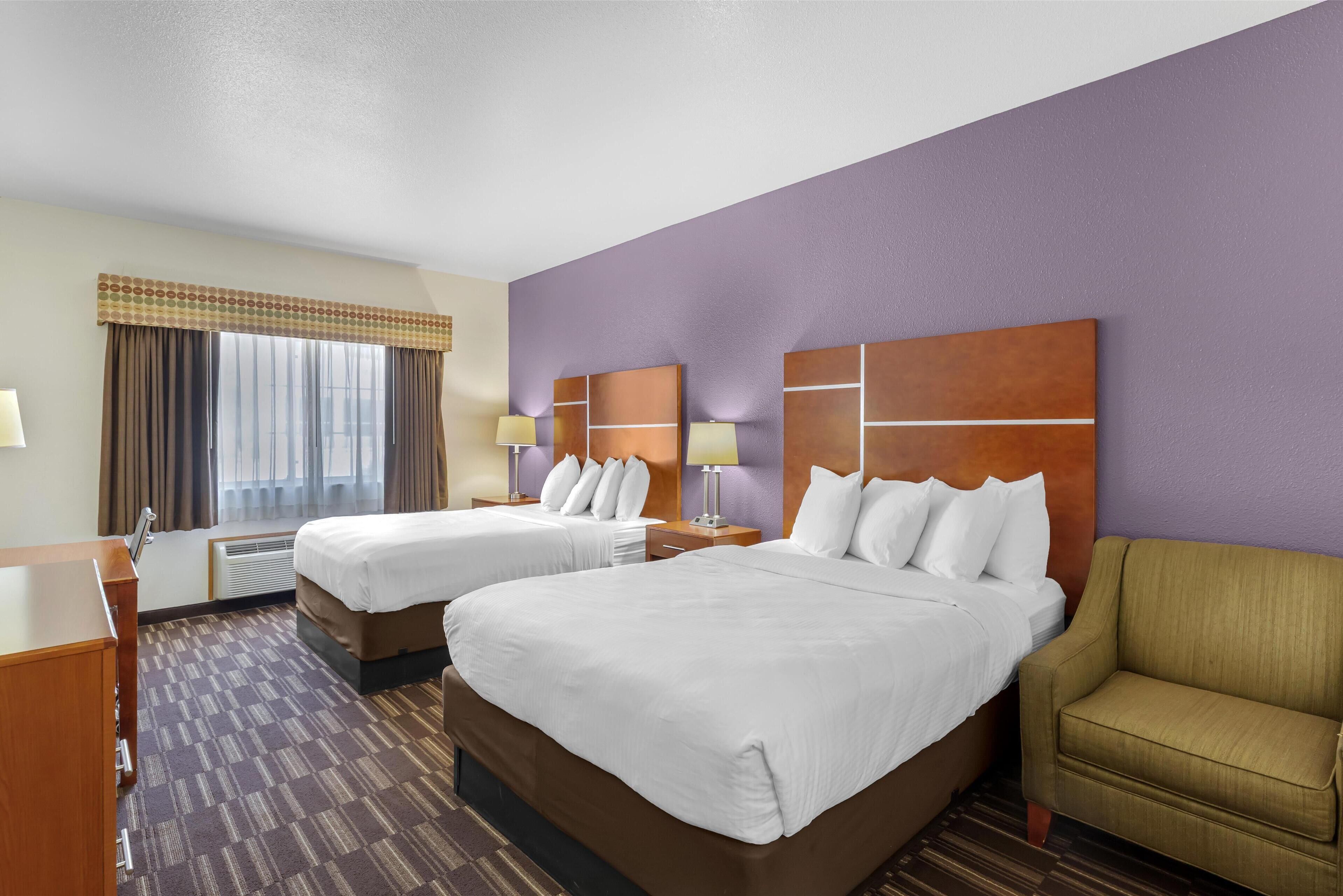 A hotel room with two beds, a desk, a chair, and a large window with curtains.