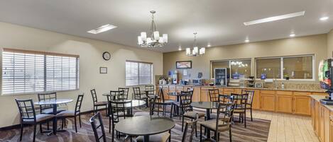 A dining area with round tables and chairs, a kitchen area with wooden cabinets, and a clock on the wall.