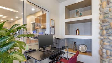 A modern office space with a desk, computer, printer, and shelves with decorative items.