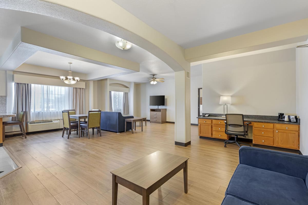 A spacious living area with a dining table, blue sofa, and a TV in the background.