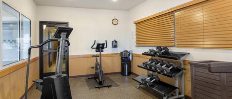 Un gimnasio con equipo cardiovascular, mancuernas y un bote de basura.