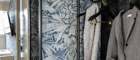 A room with a mirrored closet door, a grey coat, and a grey bag hanging on a black hanger.