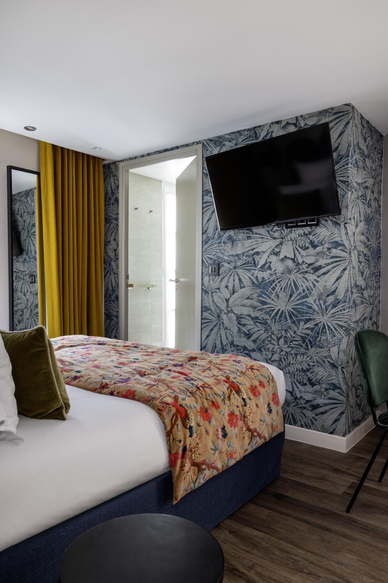 A hotel room with a bed, a TV mounted on the wall, and a window with curtains.