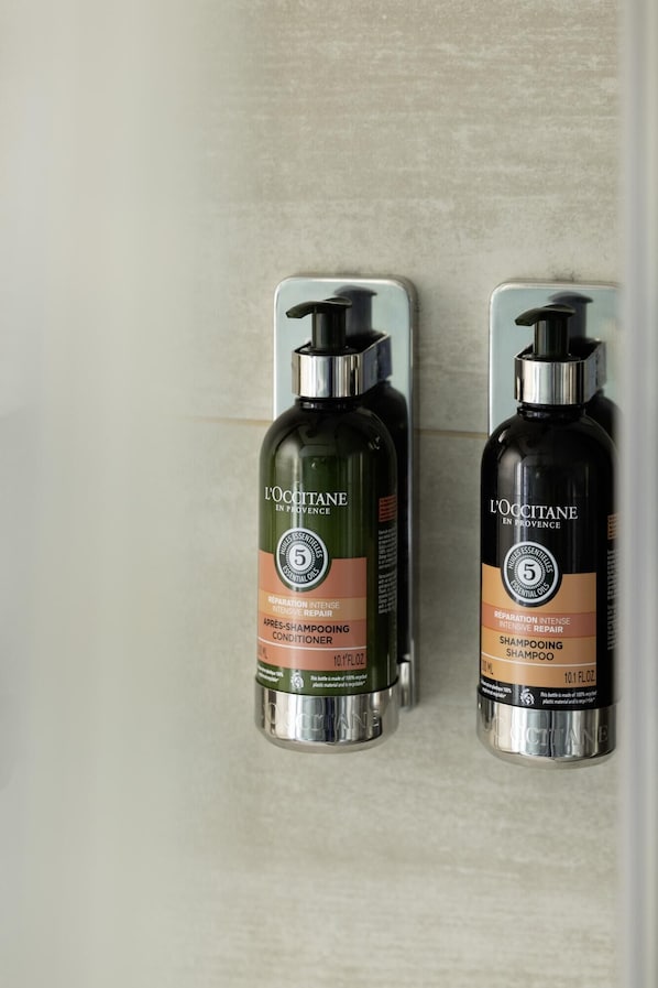 Two bottles of L'OCCITANE shampoo and conditioner on a wall-mounted dispenser.