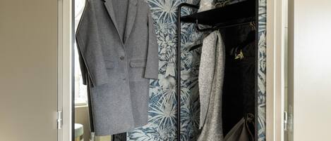 A wardrobe with a grey coat hanging on a rack, a patterned fabric, and a grey bag on a shelf.