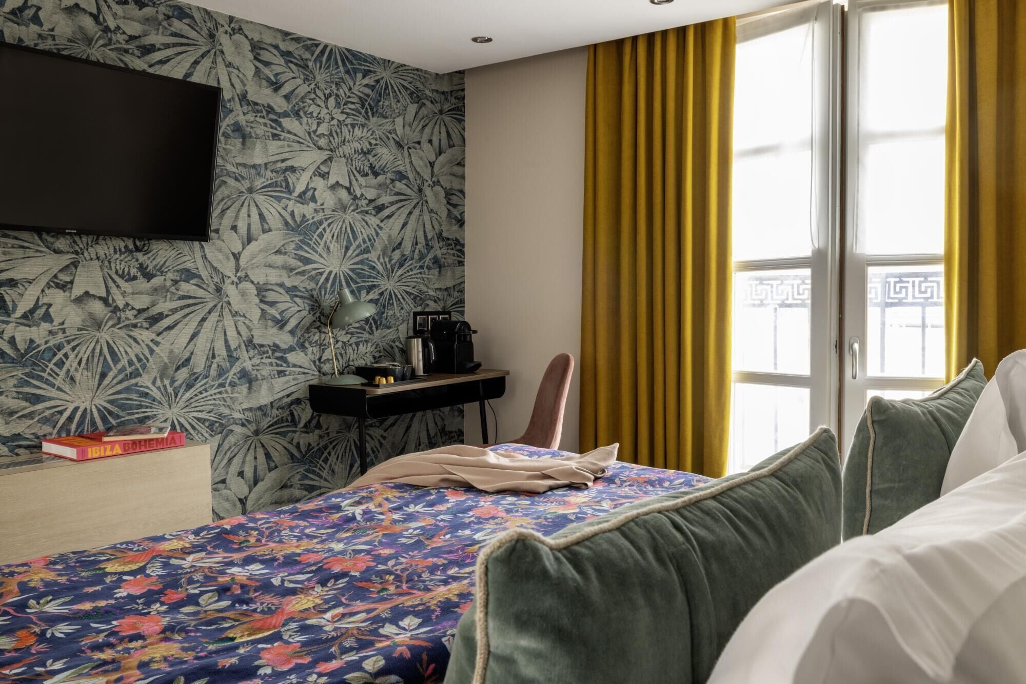 Une chambre d’hôtel avec un lit, un bureau, un téléviseur à écran plat fixé au mur et une fenêtre avec des rideaux jaunes.