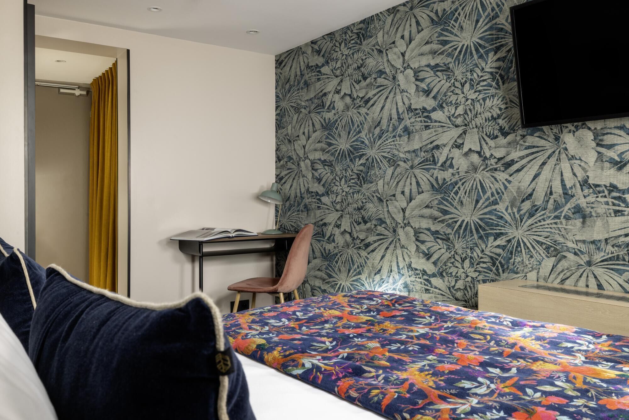 A hotel room with a bed, a desk, a chair, and a TV on the wall.
