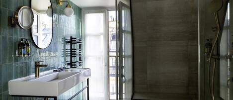 Un baño moderno con cabina de ducha de vidrio, un lavabo blanco con grifo dorado y un espejo grande con marco dorado.