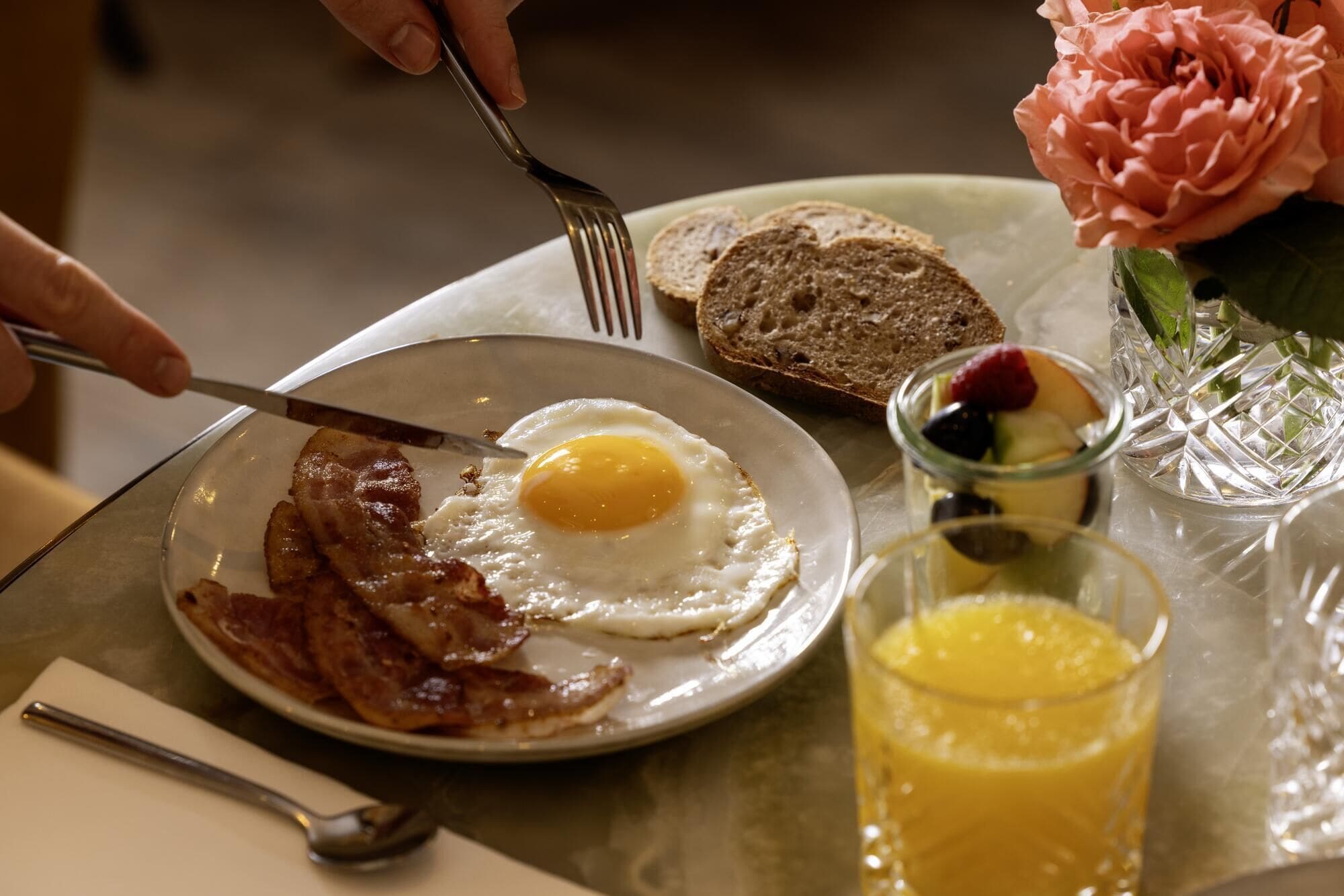 Prato de café da manhã com bacon, um ovo, torradas e um copo de suco de laranja.