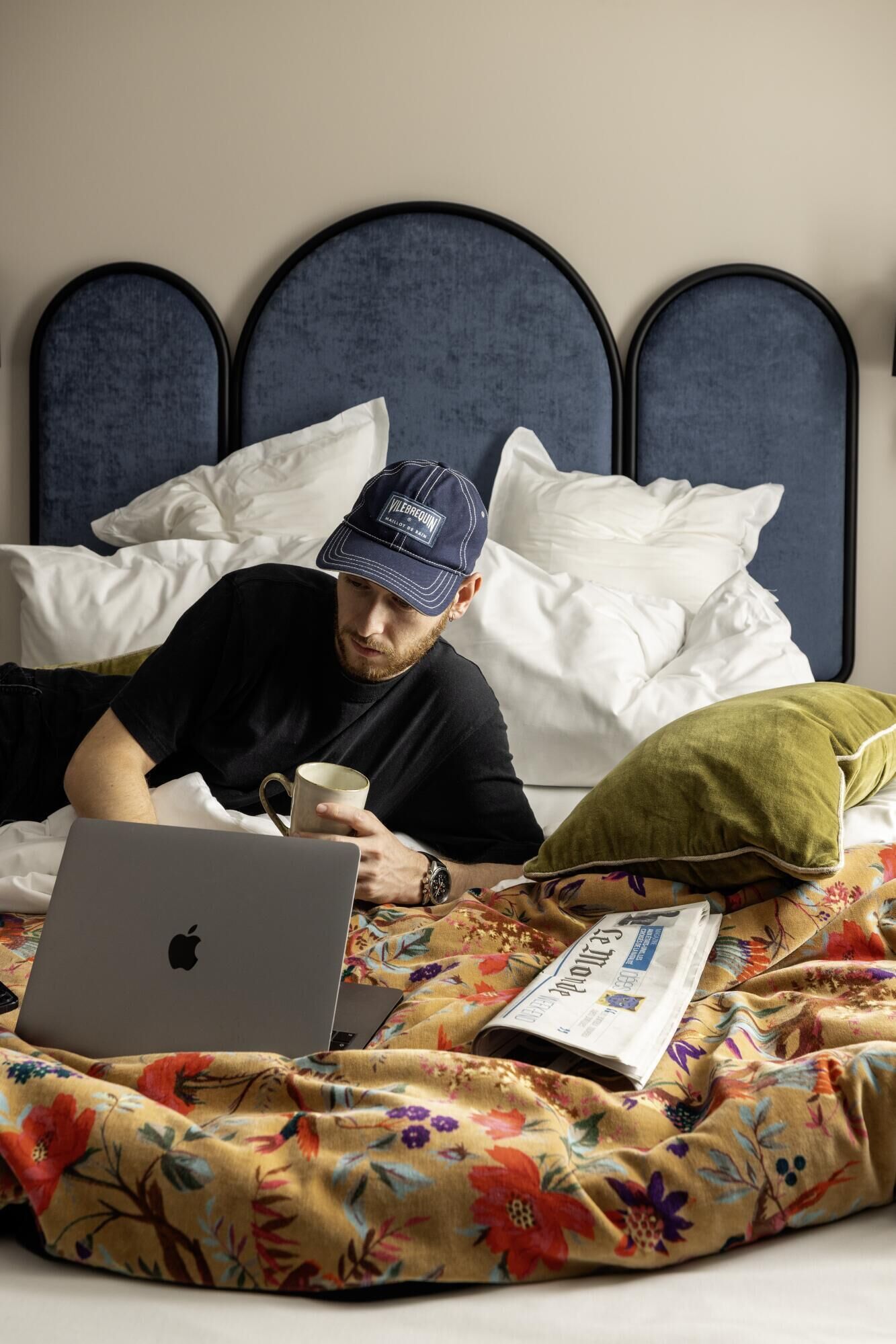 A person lying on a bed with a laptop, a cup, and a magazine.