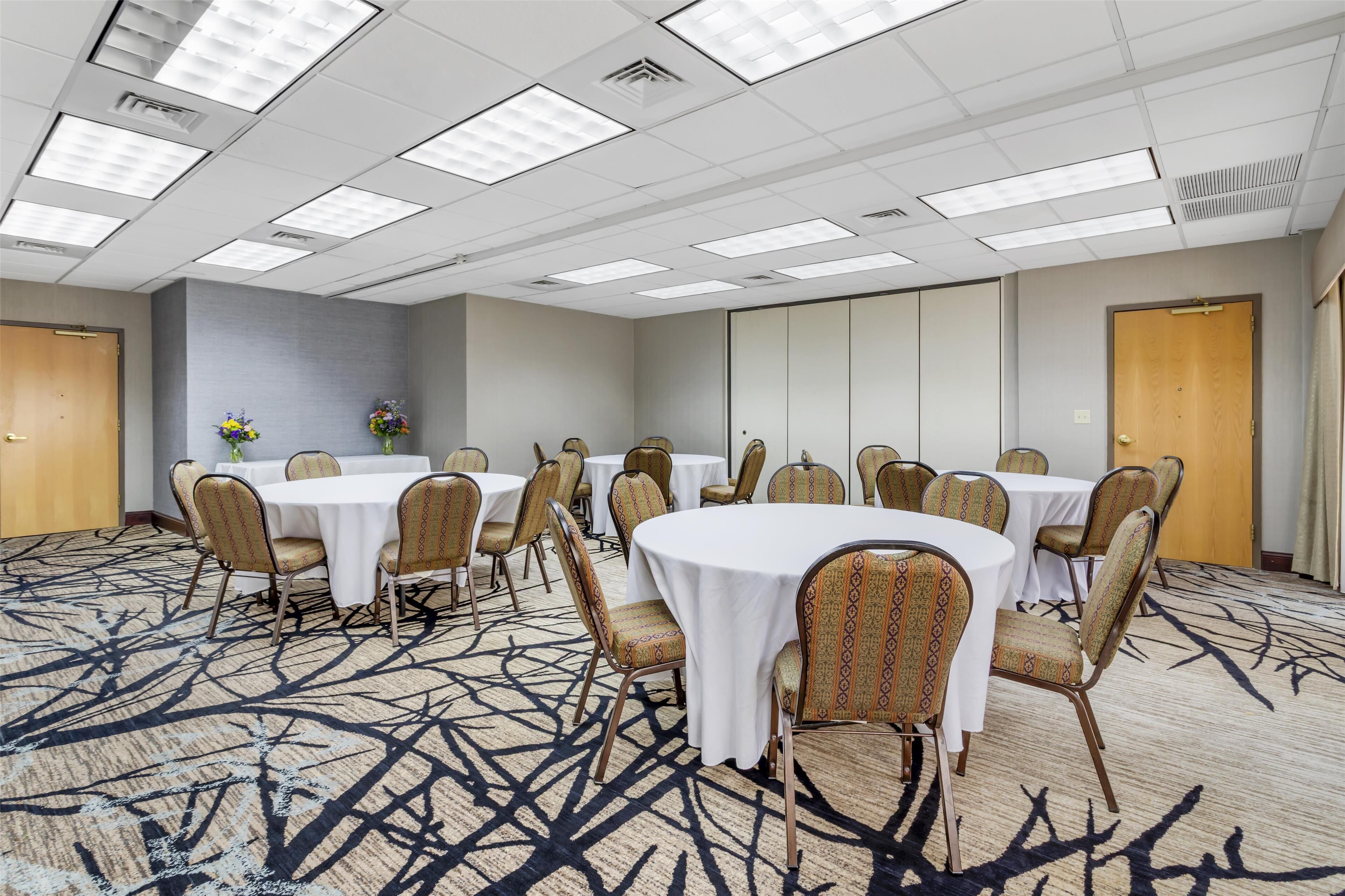 A conference room with multiple tables and chairs, a patterned carpet, and a ceiling with fluorescent lights.