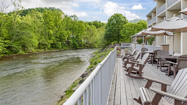 A deck with outdoor seating overlooking a river, surrounded by lush greenery and a building with balconies. - Best Western Plus River Escape Inn & Suites (Dillsboro)
