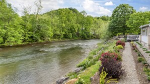 A river with a stone pathway and a building with a balcony overlooking the river. - Best Western Plus River Escape Inn & Suites (Dillsboro)