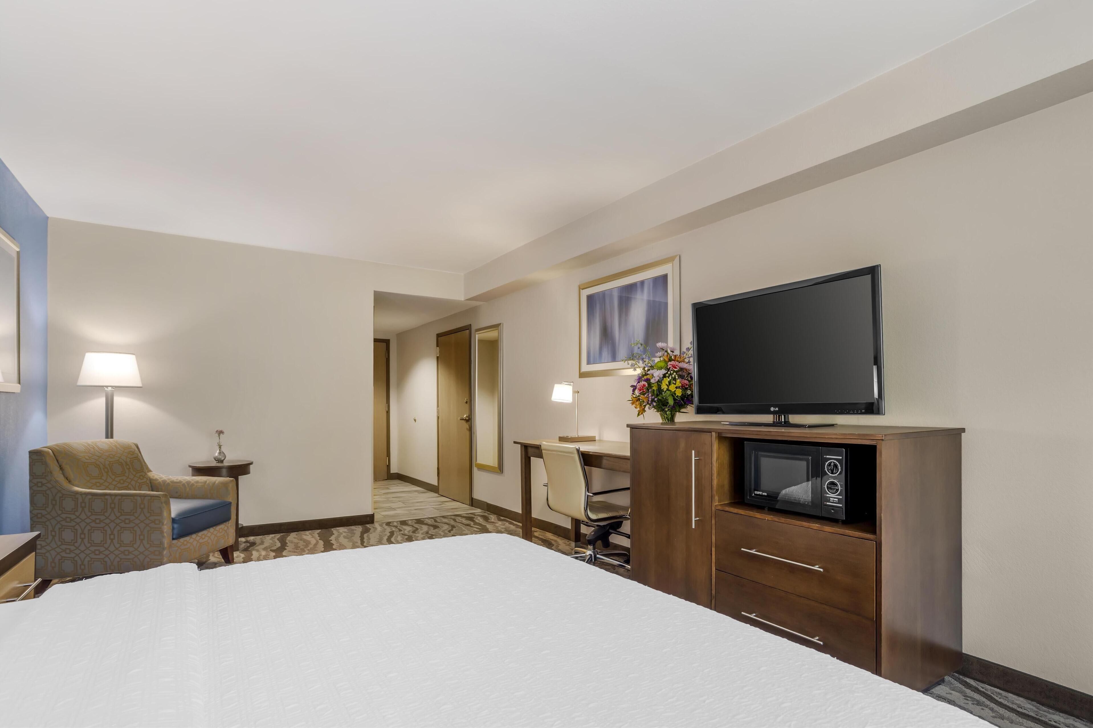 Habitació d'hotel amb un llit, escriptori, cadira, televisió, microones i una taula petita amb làmpada.