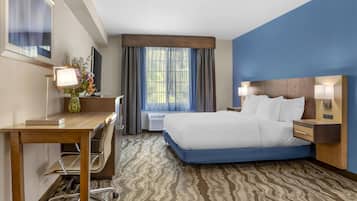 A hotel room with a large bed, a desk with a chair, a TV, and a window with curtains.