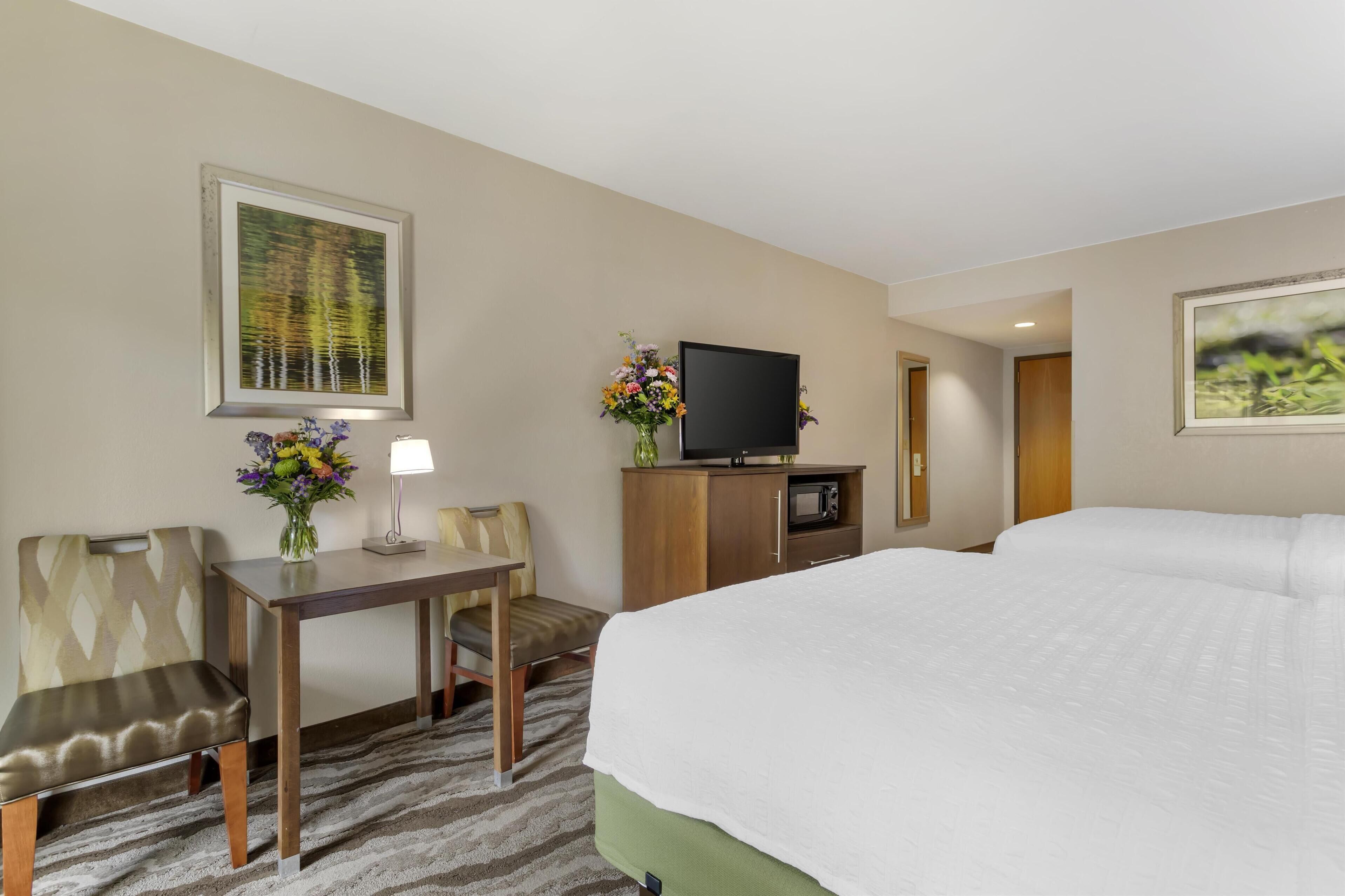 A hotel room with a large bed, a desk with a chair, a television, and a small cabinet.