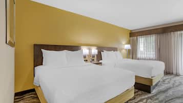A hotel room with two beds, a wooden headboard, a patterned carpet, and a window with curtains.