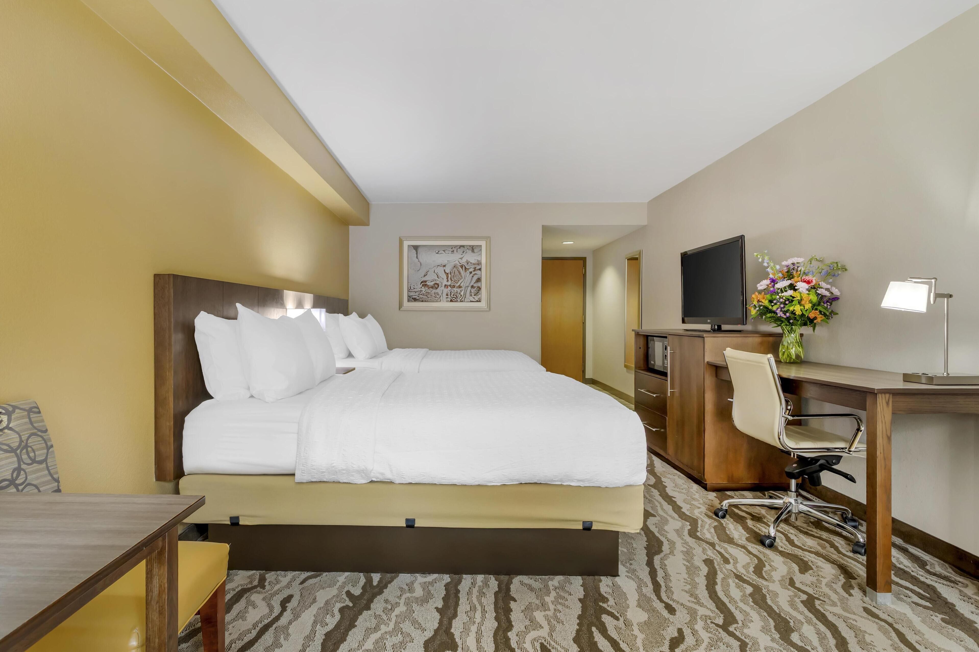 Habitación de hotel con una cama grande, un escritorio con silla, televisor y un arreglo floral.