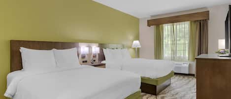 A hotel room with two beds, a wooden headboard, a nightstand with a lamp, a window with curtains, and a desk with a lamp.