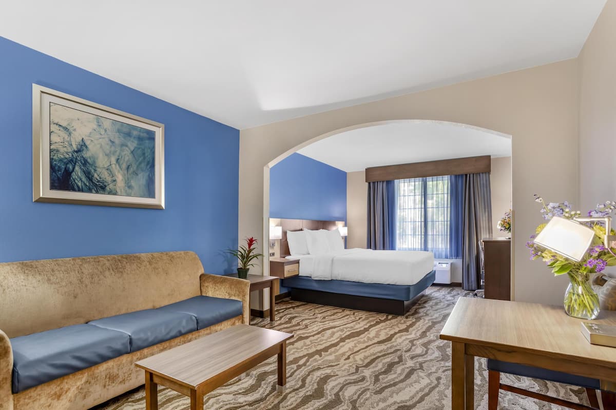 A hotel room with a sofa, a bed, a desk, and a painting on the wall.
