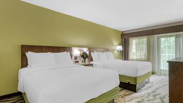 A hotel room with two beds, a nightstand with a lamp, and a view of trees through the window.