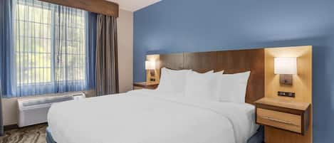 A hotel room with a large bed, two bedside tables with lamps, a window with curtains, and a wall-mounted heater.