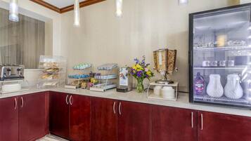 A hotel breakfast area with a refrigerator, coffee machine, and various food items.