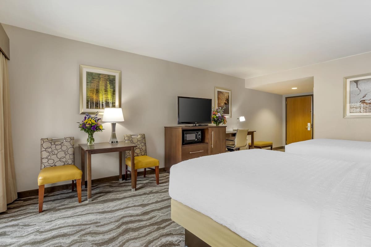 A hotel room with a large bed, a desk with a lamp, a television, and a small table with a vase of flowers.