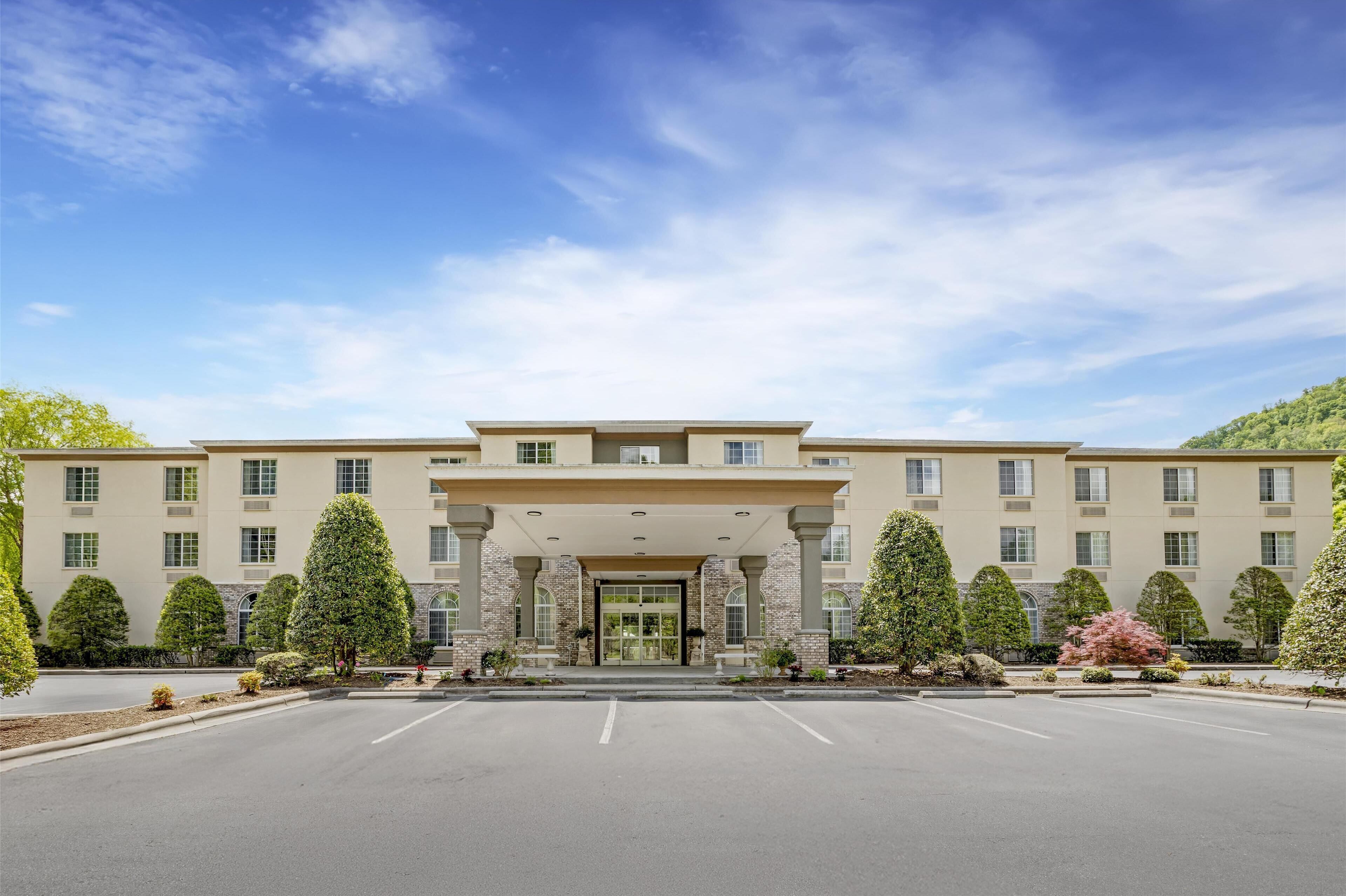 A large, multi-story hotel with a symmetrical facade, a central entrance with a covered walkway, and a parking lot in front.