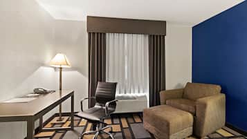 A hotel room with a desk, chair, and sofa.
