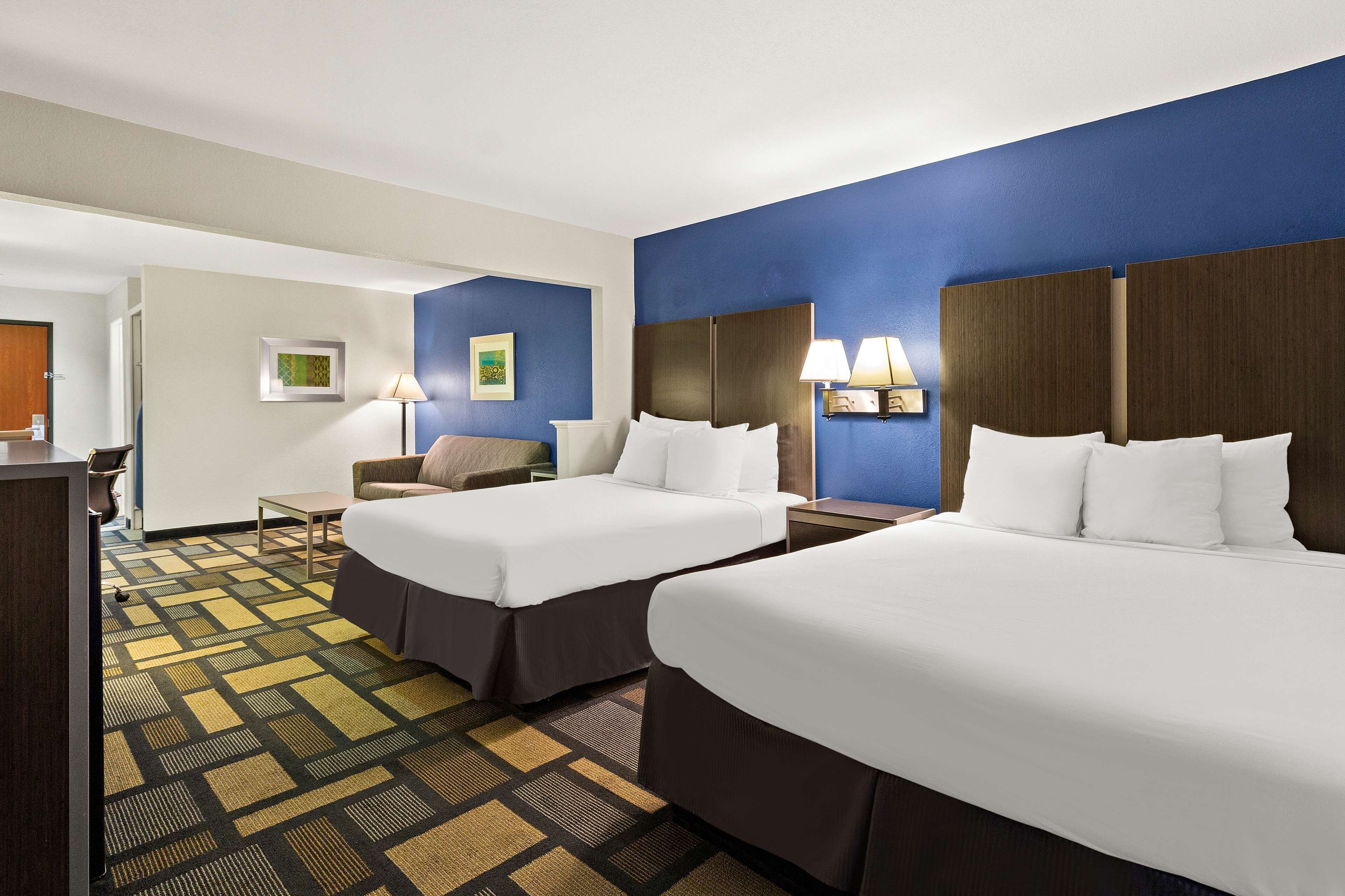 A hotel room with two beds, a desk, a chair, and a small table.