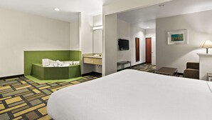 Hotellihuone, jossa on suuri sänky, vihreä oleskelualue, pieni pöytä, televisio ja taulu seinällä.