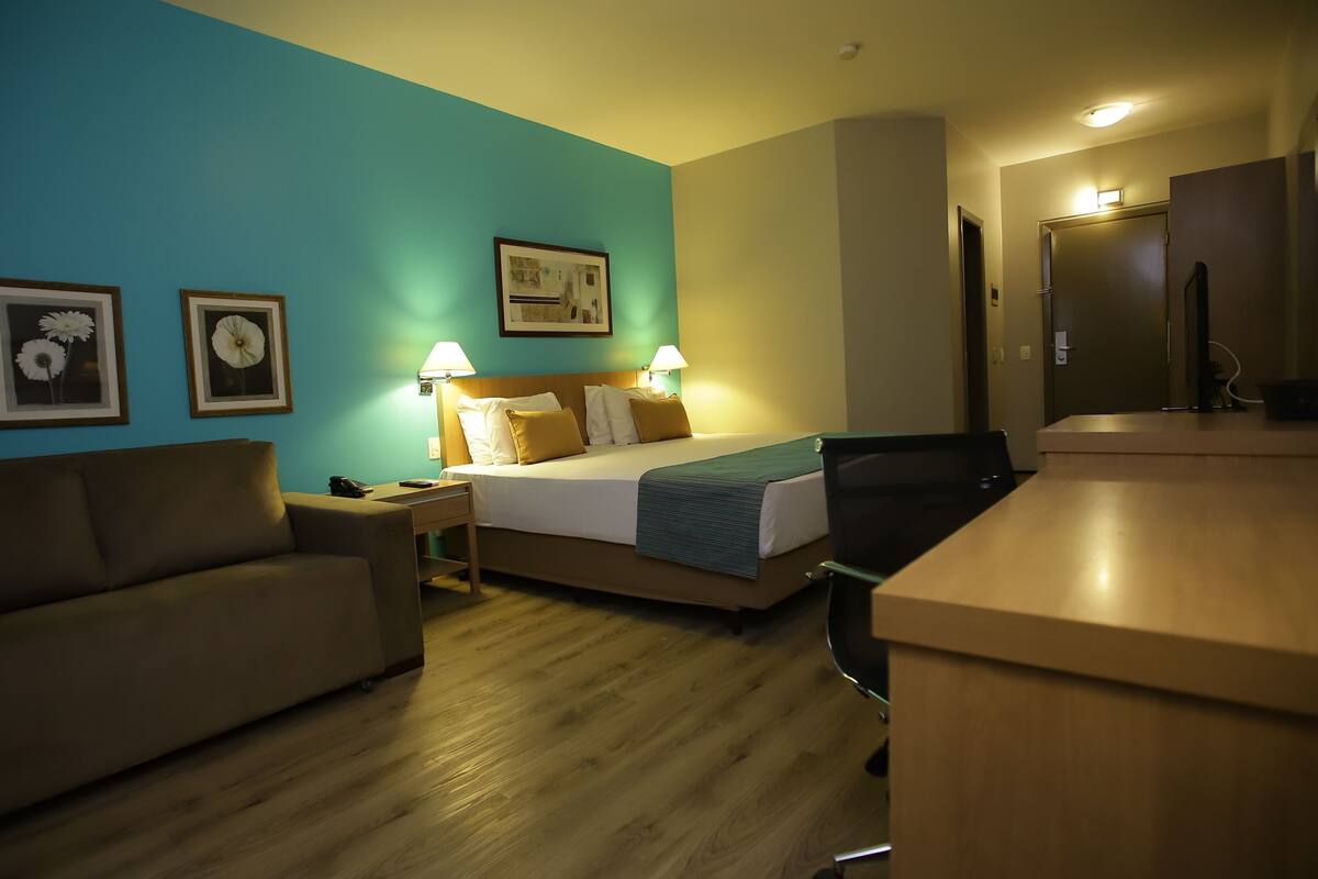 A hotel room with a bed, a desk, a chair, a sofa, and two lamps.